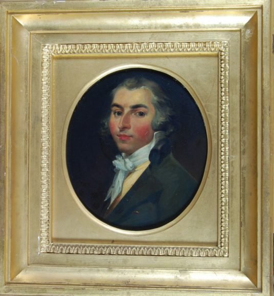 Een geschilderd portretje in gouden lijst van een glimlachende jonge man met rode wangen.