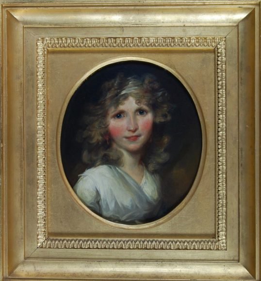 Een geschilderd portretje in gouden lijst van een glimlachende jonge vrouw met rode wangen.