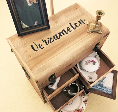 Een oude houten reiskoffer met open lades met daarin oud servies en andere items uit het Huis Van Gijn. Het portret van Simon staat boven op de koffer