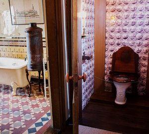 Doorkijkje naar het toilet en de badkamer. Beide kamers zijn betegeld met versierde tegels. Naast het bad staat een ketel.