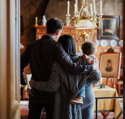 Man slaat arm om vrouw en kindje. Ze kijken een kamer in Huis Van Gijn in.