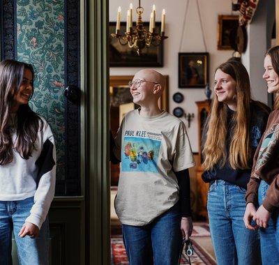 Vier jonge vrouwen staan in de gang van Huis Van Gijn. Ze lachen en praten met elkaar.