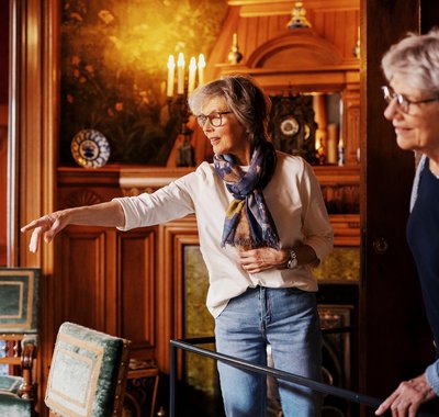 Twee dames bekijken een kamer in Huis Van Gijn. Ze lachen en een vrouw wijst iets aan.