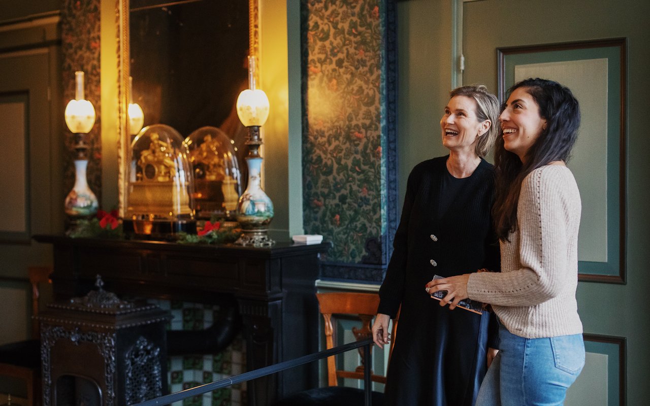 Twee vrouwen staan lachend in een kamer in Huis Van Gijn.