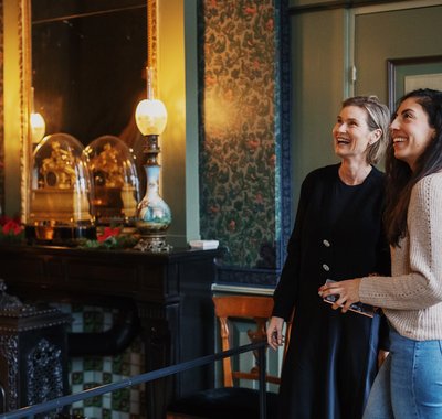 Twee vrouwen staan lachend in een kamer in Huis Van Gijn.