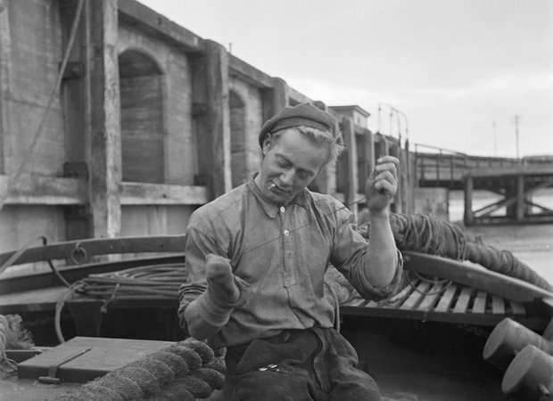 Nationaal archief - Bemanningslid van een baggerschip in de haven van Rosslare bezig met sokken stoppen. - 1932