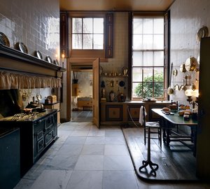 19de eeuwse keuken. Tegels op de vloeren, koperen potten en pannen. Een groot fornuis.