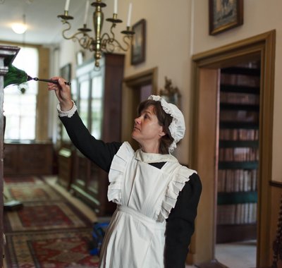 Een dienstmeid stoft een kast af in de hal van Huis Van Gijn.