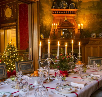 Een sfeervol gedekte tafel met kandelaars in Huis Van Gijn.. Er staat een kerstboom in de kamer.