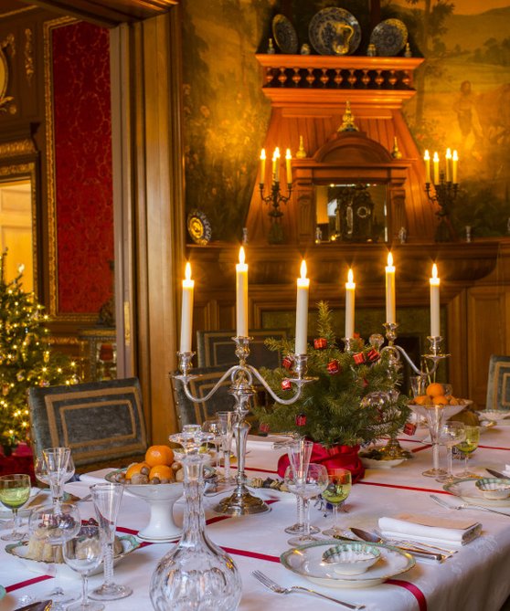 Een sfeervol gedekte tafel met kandelaars in Huis Van Gijn.. Er staat een kerstboom in de kamer.